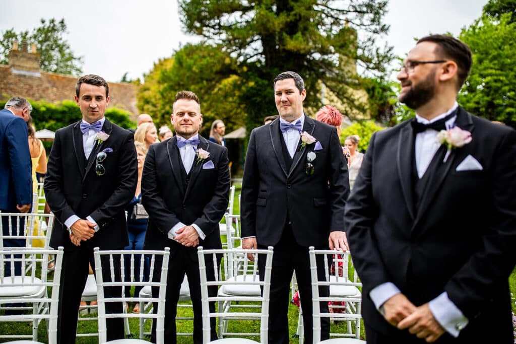 Groom and groomsmen at end of aisle in outdoor garden wedding ceremony waiting for bride to arrive