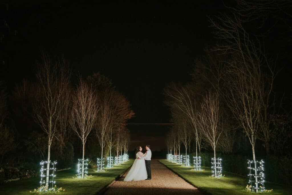 Bride and groom at night time on fairylit treelined driveway at Jewish wedding venue