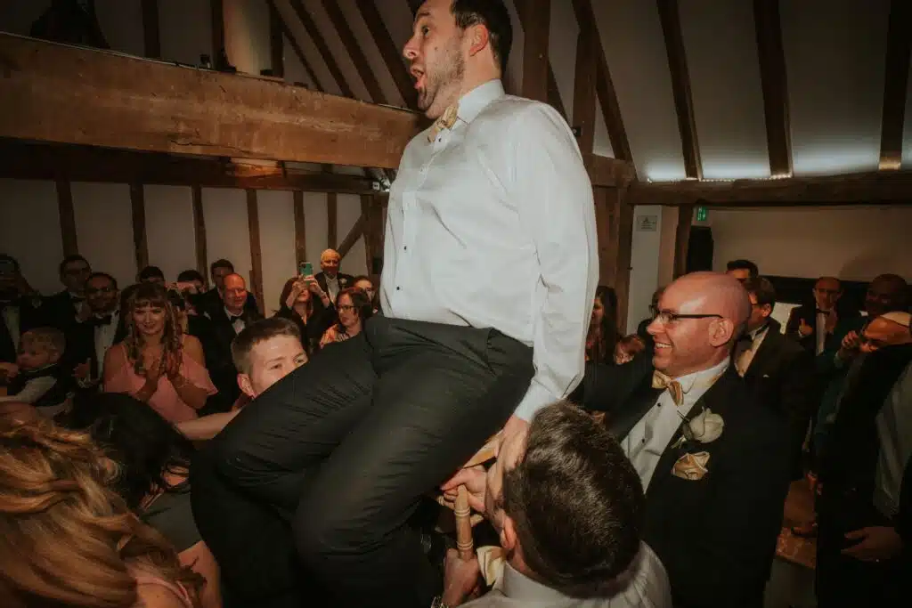 Jewish wedding celebration groom is lifted on a chair in barn wedding venue 