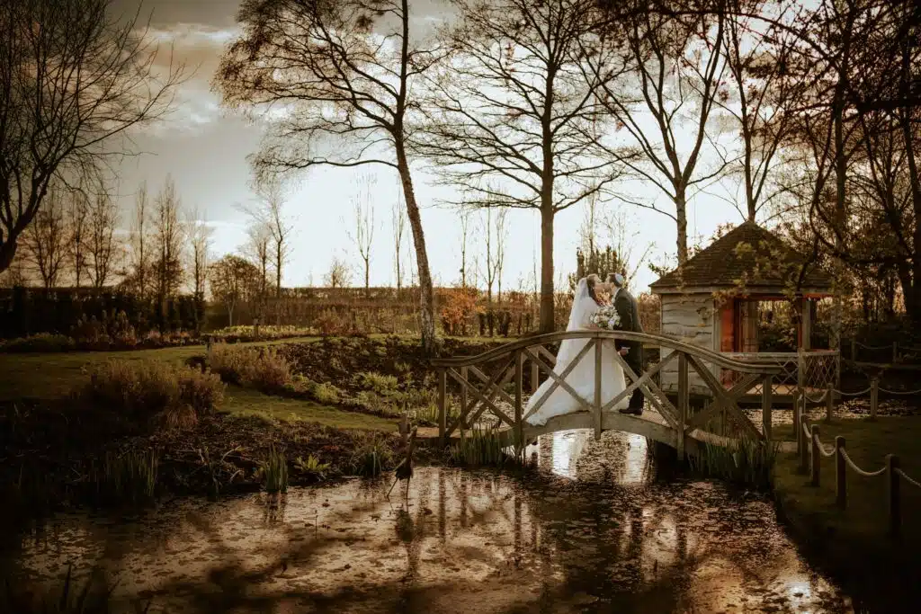 Bride and groom at Jewish wedding in garden on bridge over pretty pond 