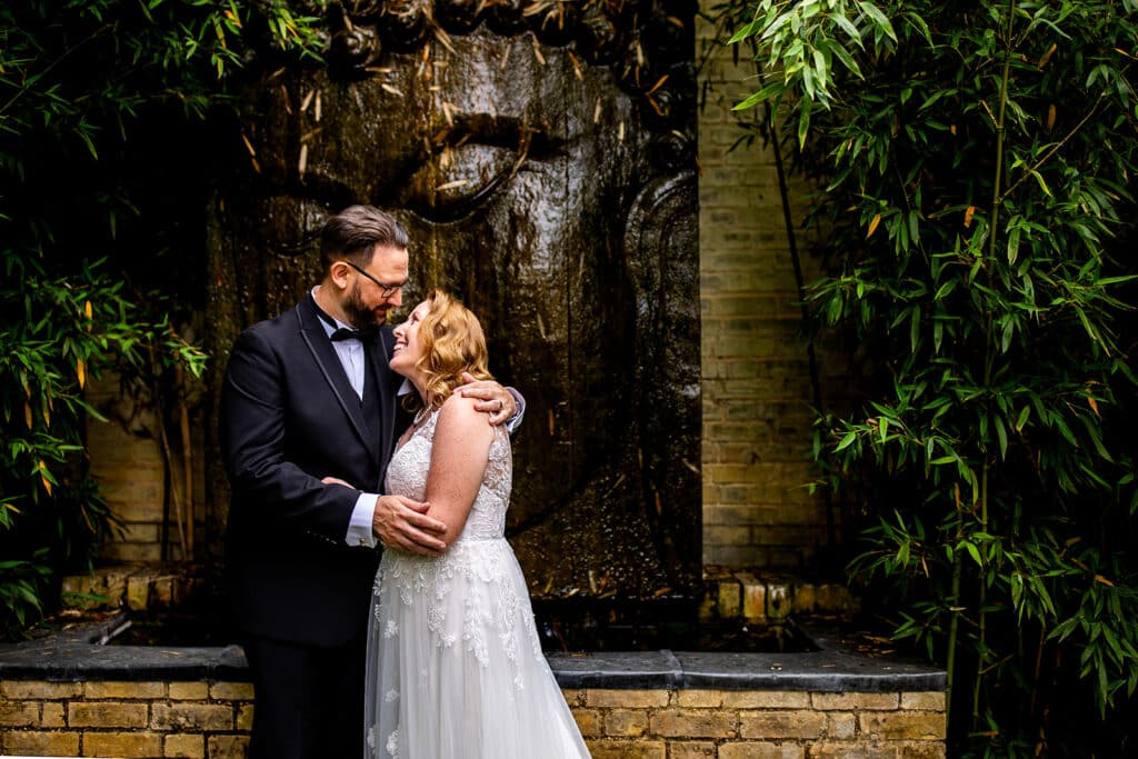 Bride and Groom at garden wedding venue in front of stone facade water feature