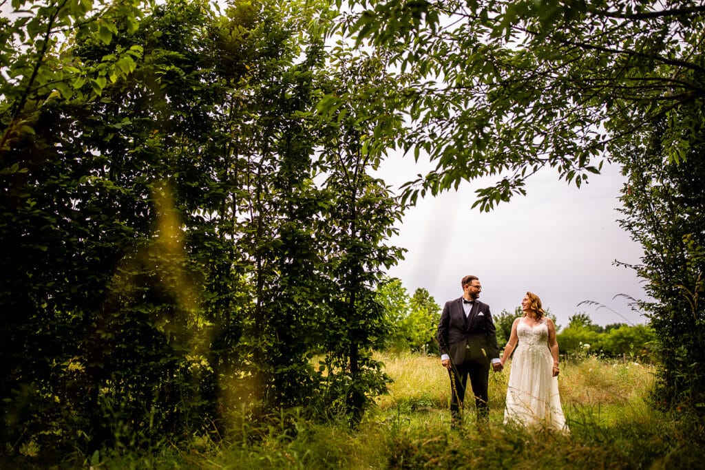Bride and groom at outdoor wedding venue under beautiful rustic tree arch with yellow fields in background