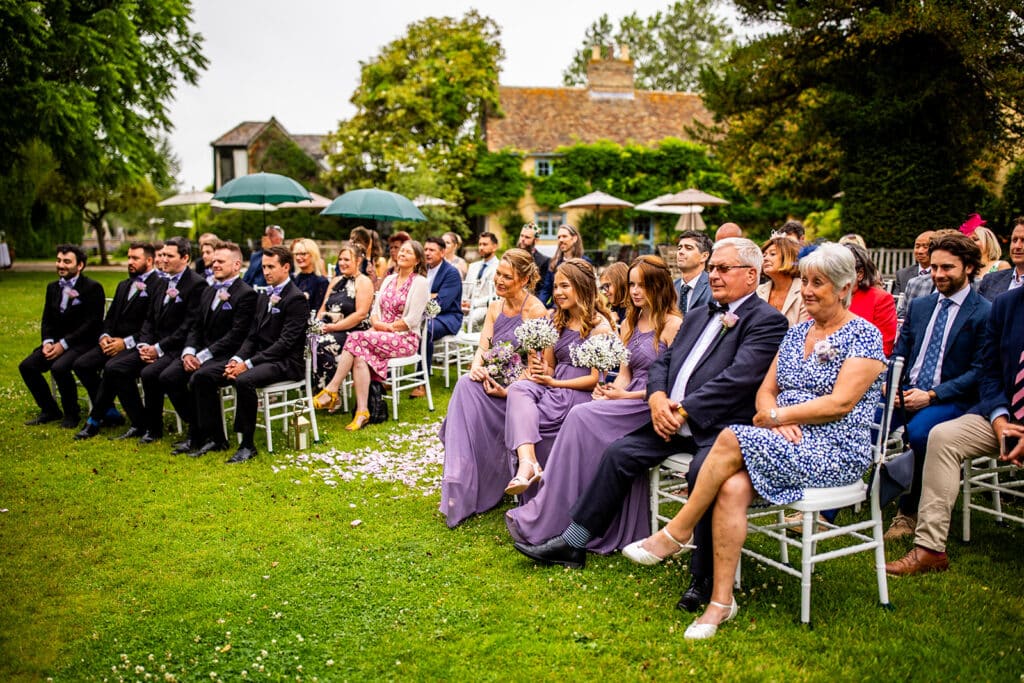 Guest seated on white chairs on lawn in outdoor garden wedding ceremony 