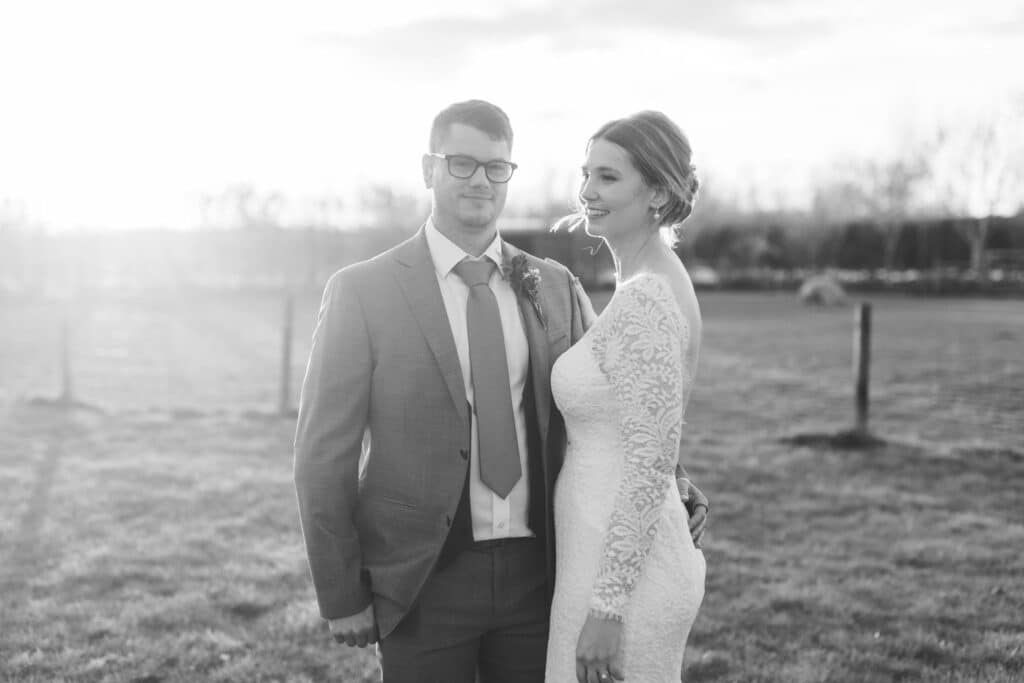 Black and white photo of bride and groom on wedding day in front of farm paddocks at countryside wedding venue