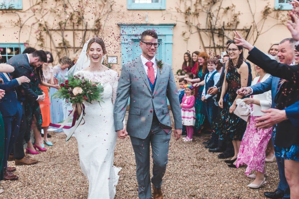 Confetti shower for bride and groom in front of pretty cream farmhouse with blue front door