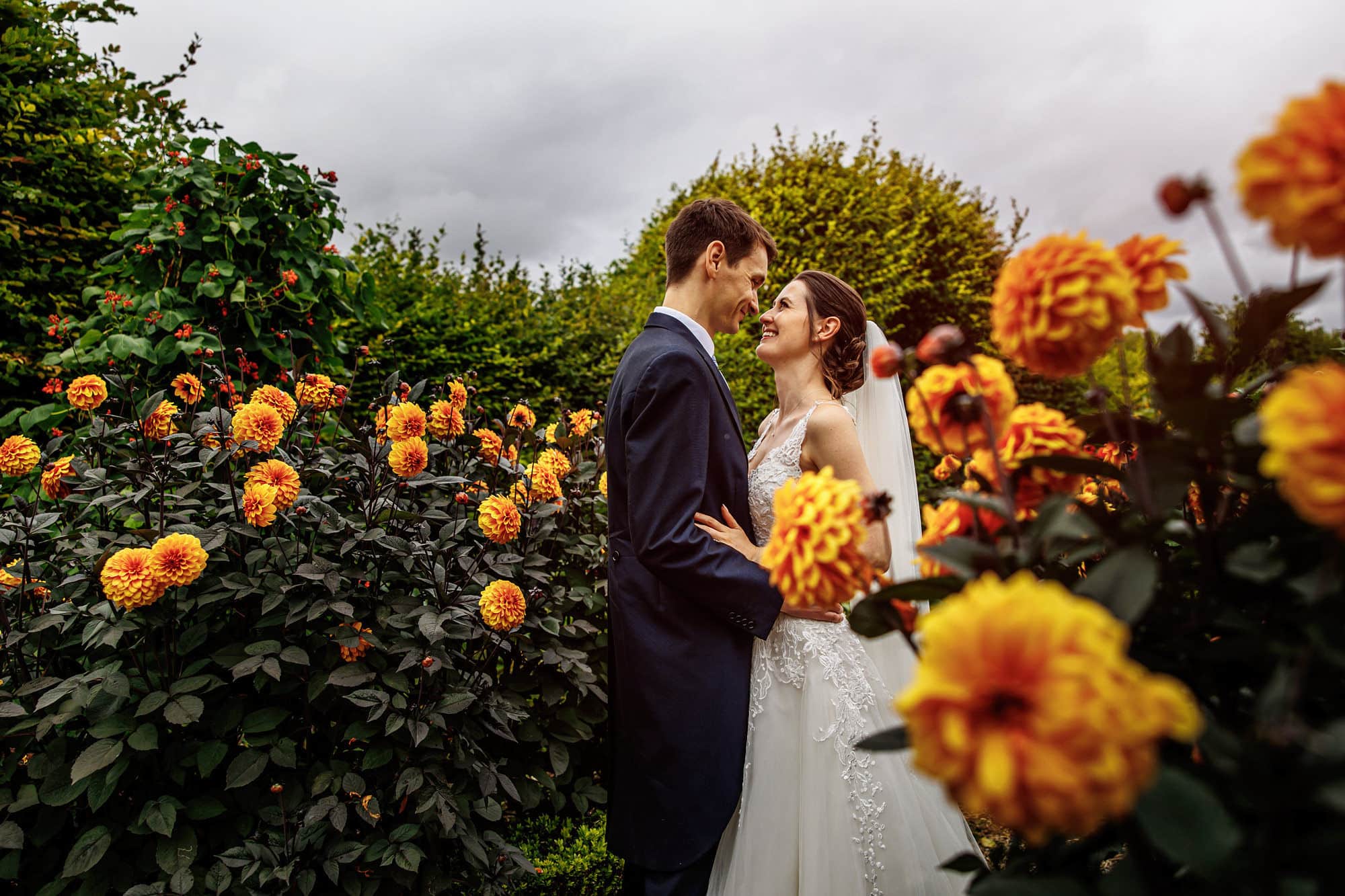 Bride and groom on wedding day surrounded by orange Dahlias in garden