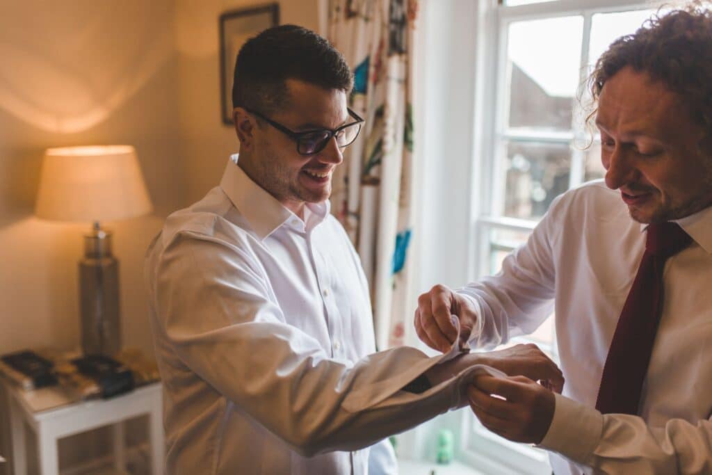 Groomsmen helps groom with cufflinks on wedding day