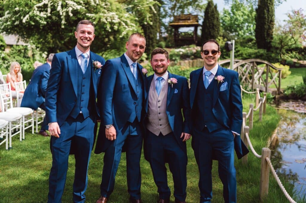 Groom and ushers in blue suits pose for photo in garden of wedding venue 