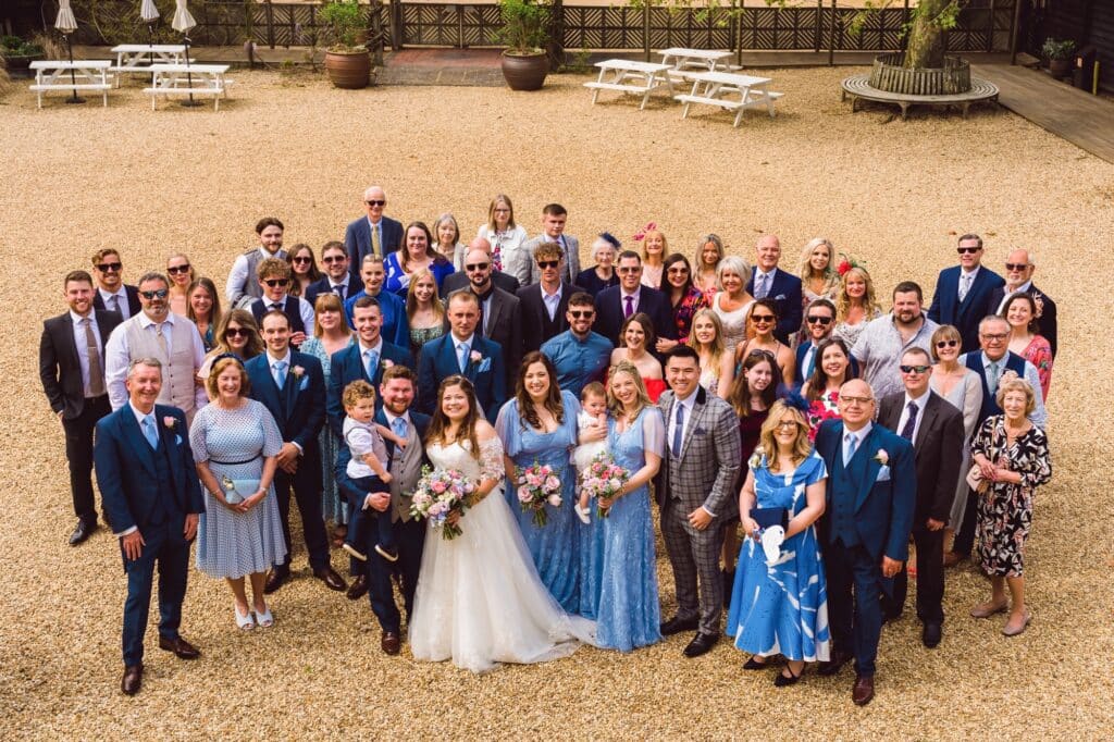 Bride and Groom surrounded by their family on friends pose for celebratory group photo in courtyard of farm wedding venue