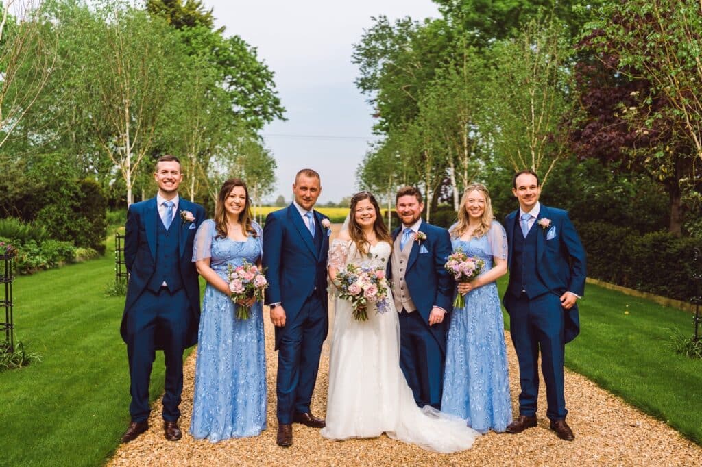 Bride and groom with bridal party on tree lined driveway of outdoor wedding venue 