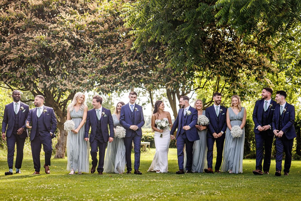 Bridal party in front of pretty trees in summer wedding garden