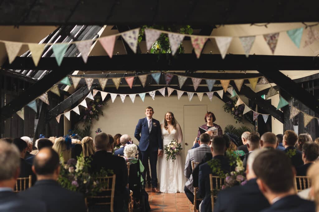 Barn wedding with pretty pastel bunting and guests looking on as couple wait to walk down the aisle 