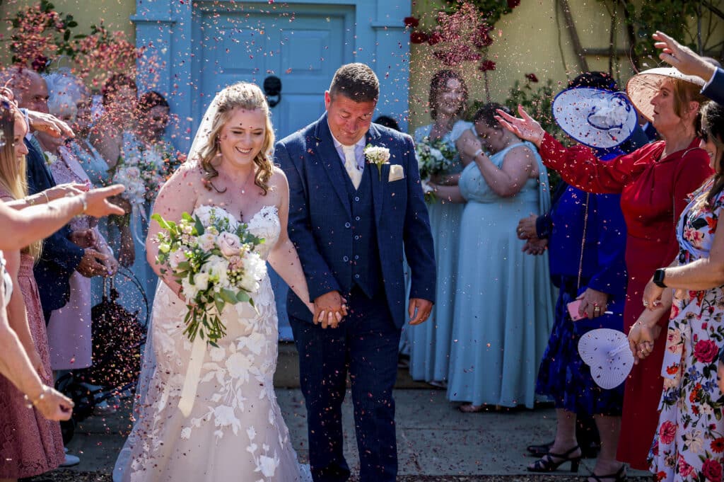 Bride and groom at country house wedding venue on sunny wedding day enjoy confetti shower 