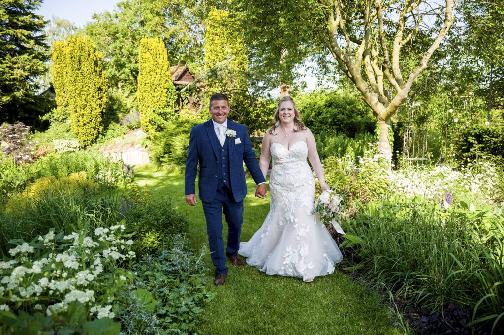 Bride and groom on sunny wedding day walk hand in hand in beautiful wedding venue gardens 