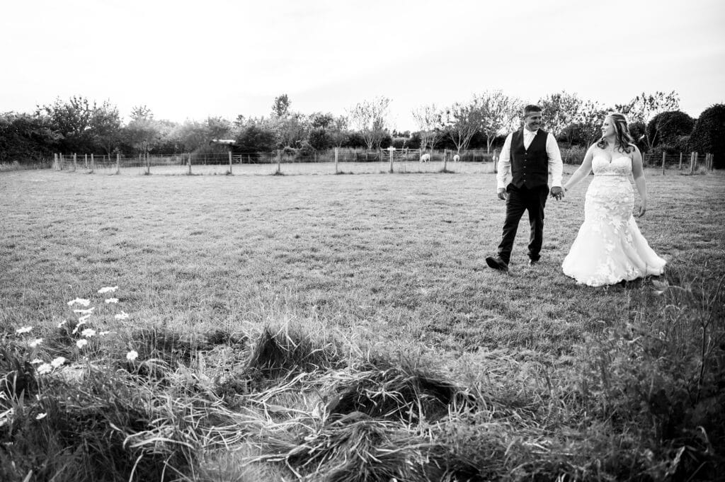 Bride and groom wander hand in hand through meadow at farm wedding venue