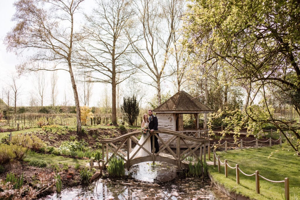 Bride and groom on bridge across pond at countryside garden wedding venue