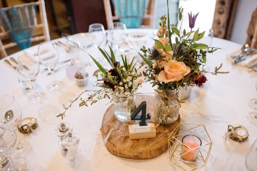 Wedding flower table centrepiece set on rustic log round at barn wedding venue