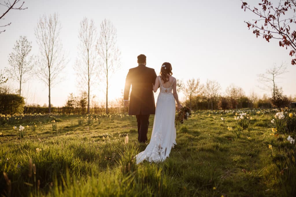Bride and groom walking away from camera at sunset in meadow at countryside wedding venue