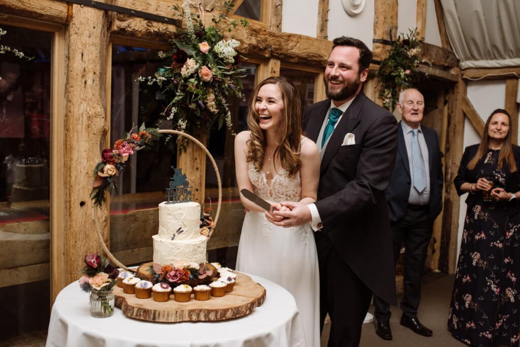 Laughing bride and groom about to cut wedding cake at barn wedding venue