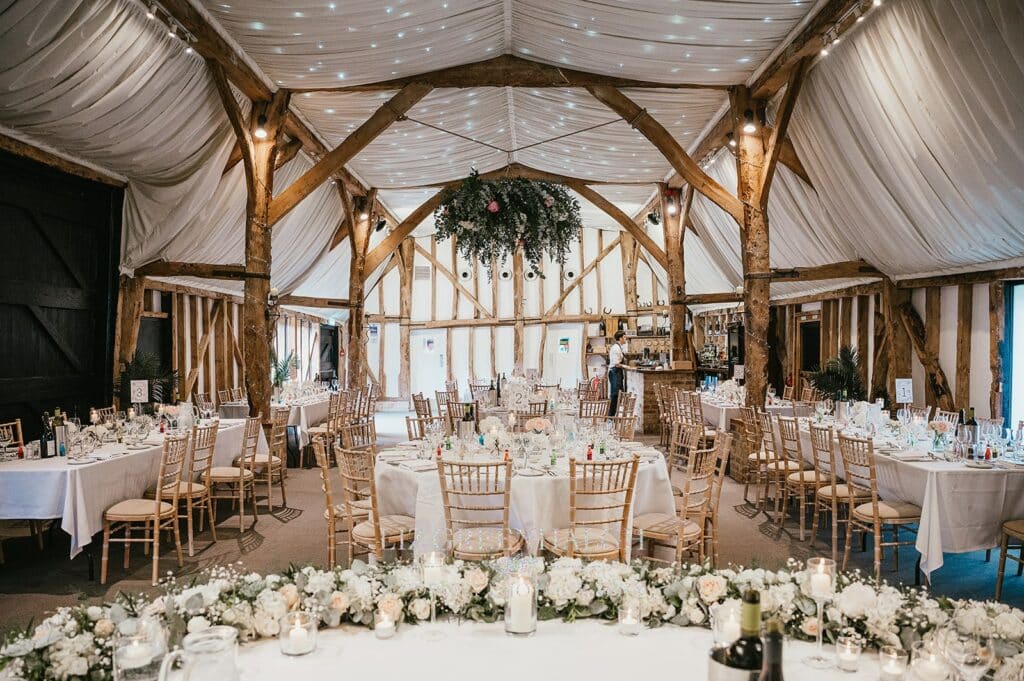 Barn Wedding Venue set for dining with beautiful ceiling floral decorations and flowers on tables
