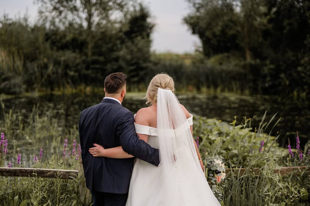 Bride and Groom with backs to camera on wedding day looking over pond at countryside wedding venue