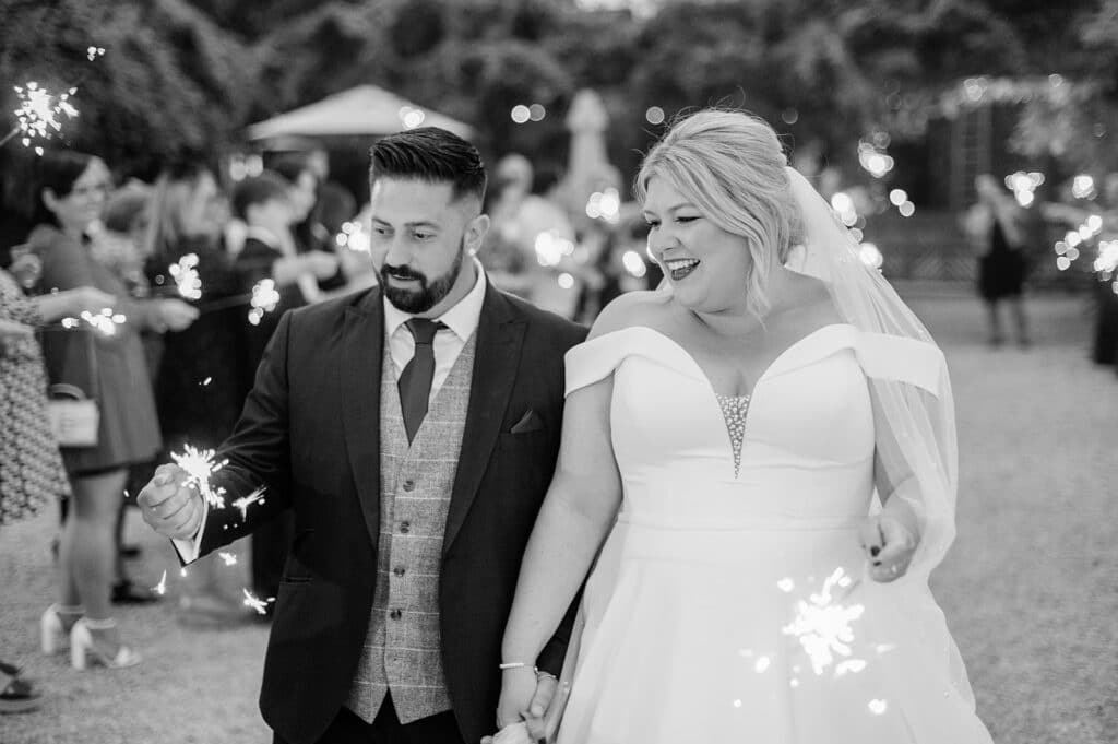 Black and white photo of bride and groom on wedding day with sparklers in courtyard of countryside wedding venue