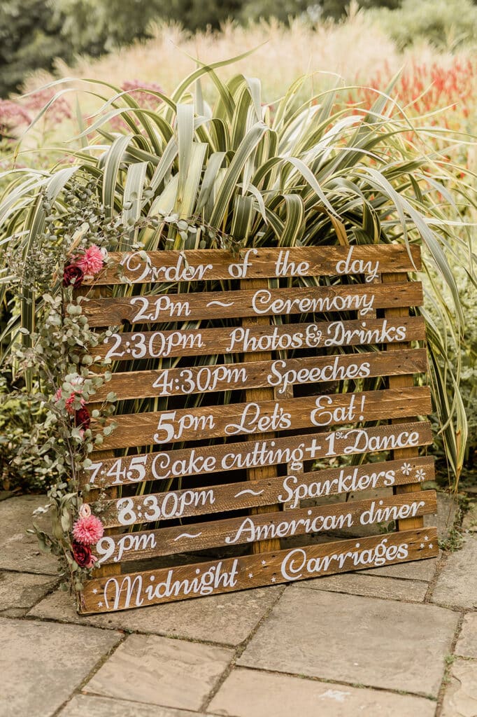 Hand painted pallet sign with order of the day in front of plants at garden wedding venue
