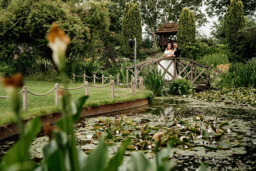 Bride and Groom in countryside wedding venue on bridge over pond on summer day 