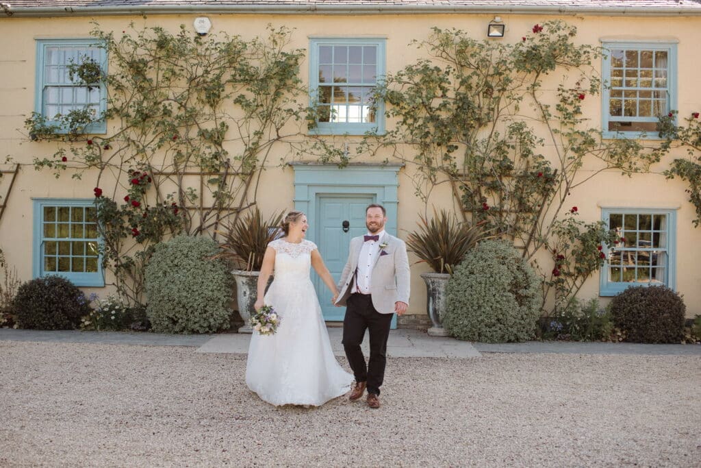 Bride and Groom on Wedding day in front of pretty country cream coloured farmhouse with blue doors and windows 