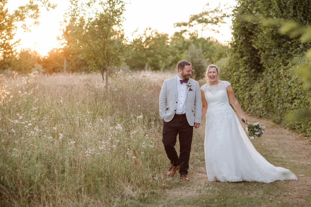 Bride and groom wander through wildflower meadows at countryside wedding venue 