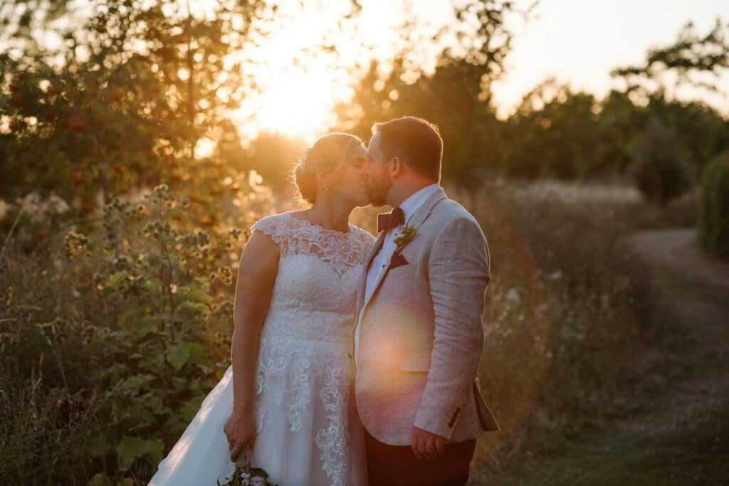 Bride and groom kiss in gardens of rustic wedding venue on their wedding day 