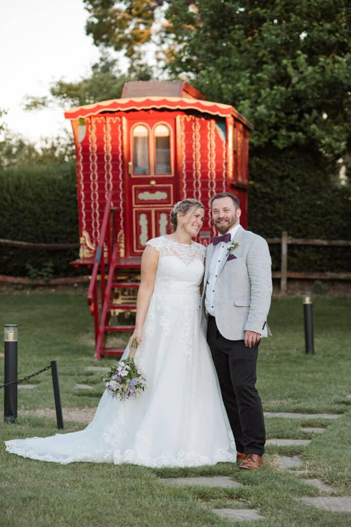 Bride and groom on wedding day in front of colourful red Romany wagon