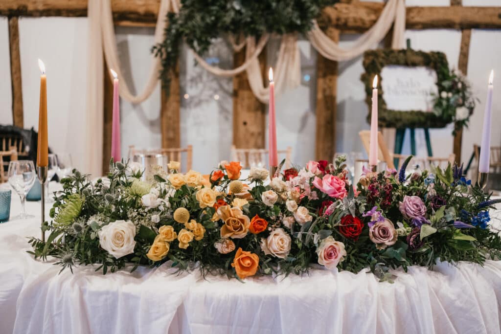 Top Table at Barn wedding venue styled with colourful flowers and beautiful peach on wooden beams behind 