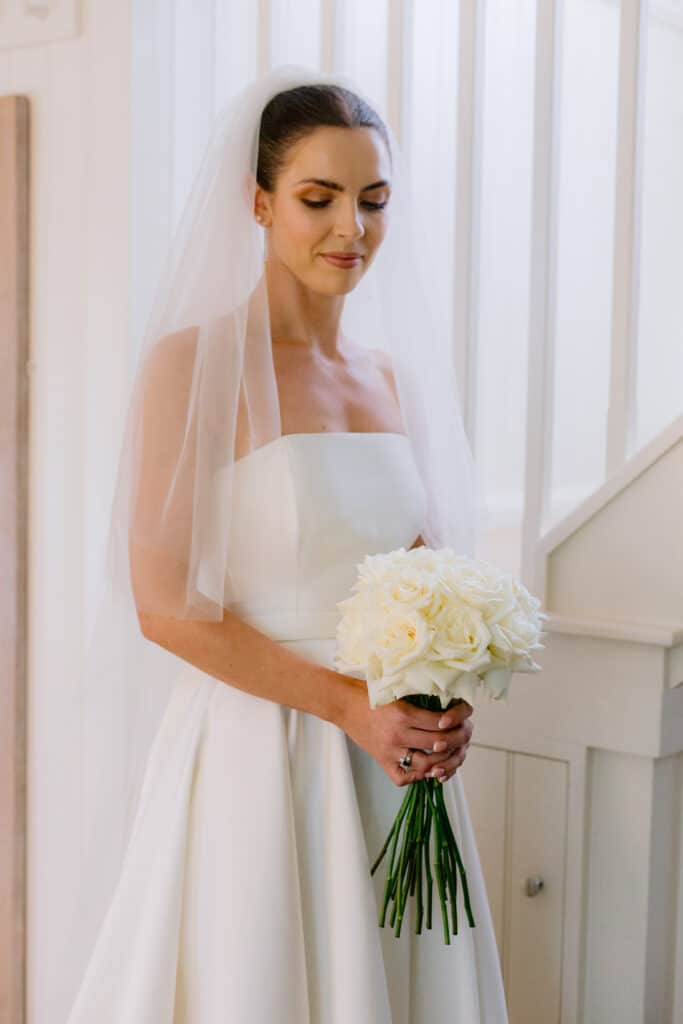 Bride in her wedding dress carrying white roses in bridal suite