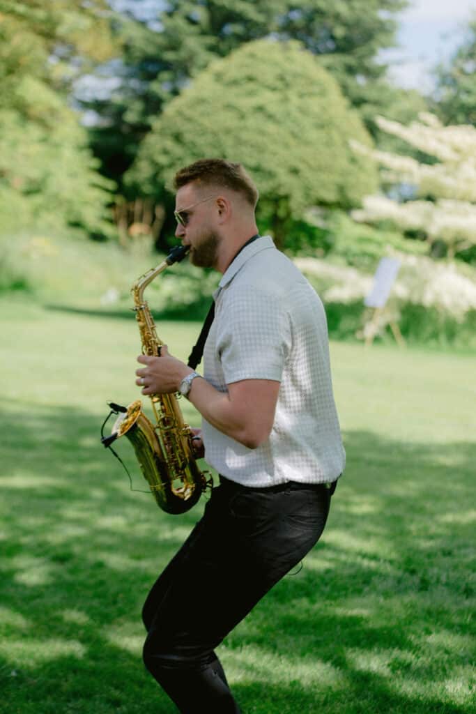 Saxophonist playing outside for drinks reception at countryside wedding venue