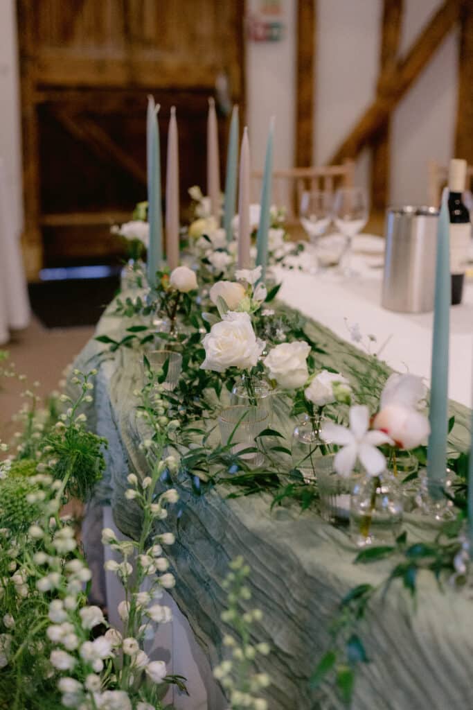 Stylish white florals and sage green tablescape in rustic barn wedding venue for wedding meal. 