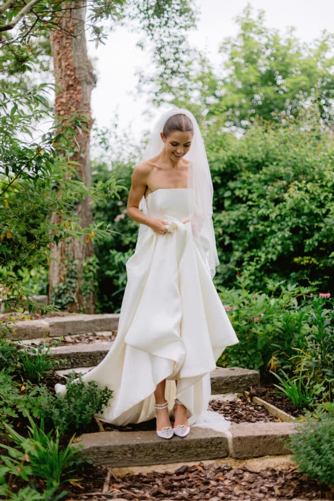 Bride in white stylish wedding dress showing off her heels in outdoor garden wedding venue