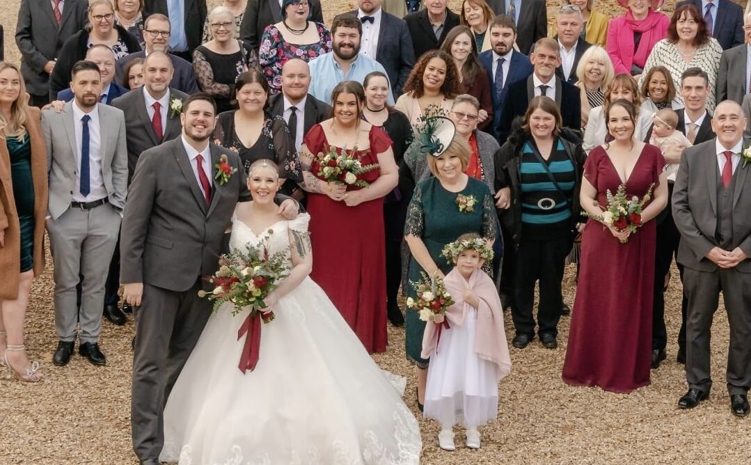 Bride and Groom pose smiling for photo with wedding guests in courtyard at farm wedding venue