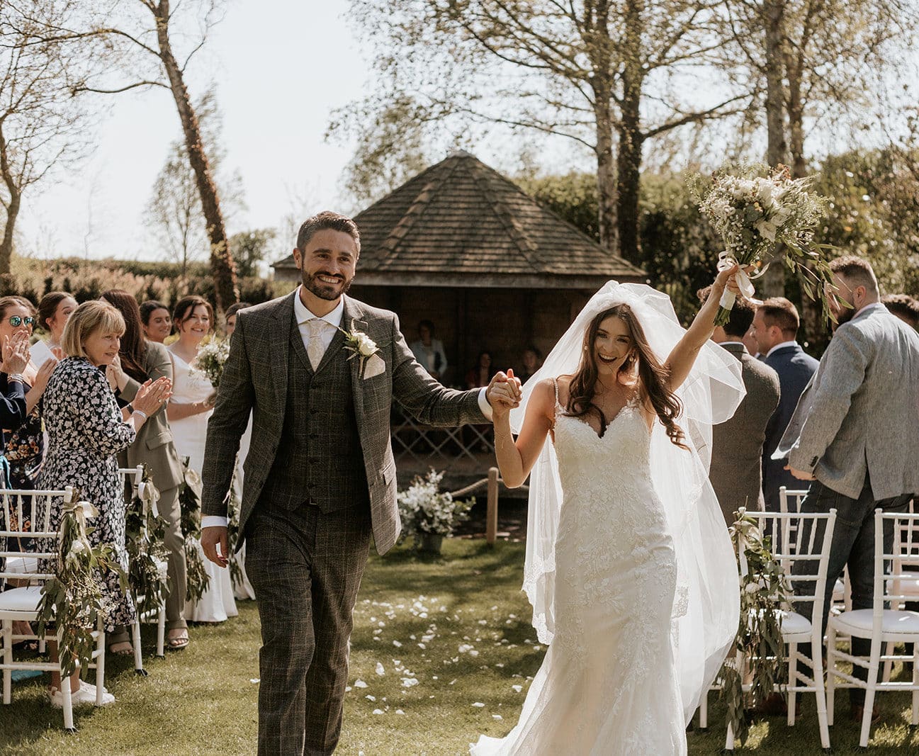 Just married bride and groom at Garden Wedding Venue Leave Ceremony and bride celebrates by raising bouquet
