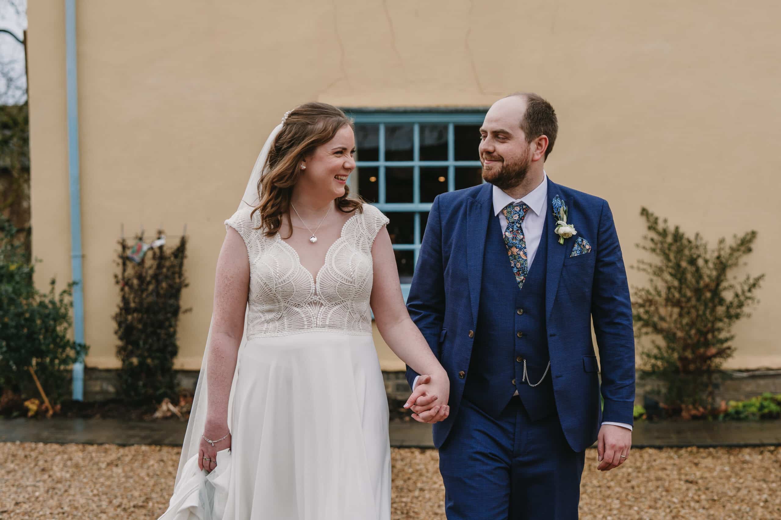 Bride and groom walk hand in hand in front of country house wedding venue