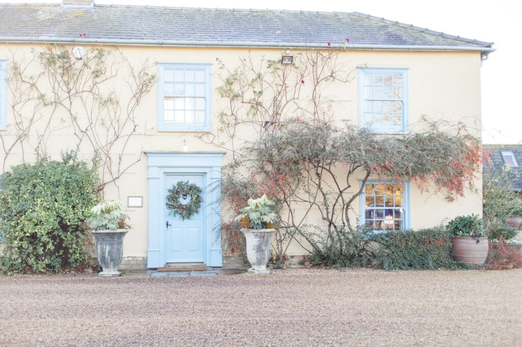 Pretty cream farm house with pale blue door and christmas wreath hanging on door