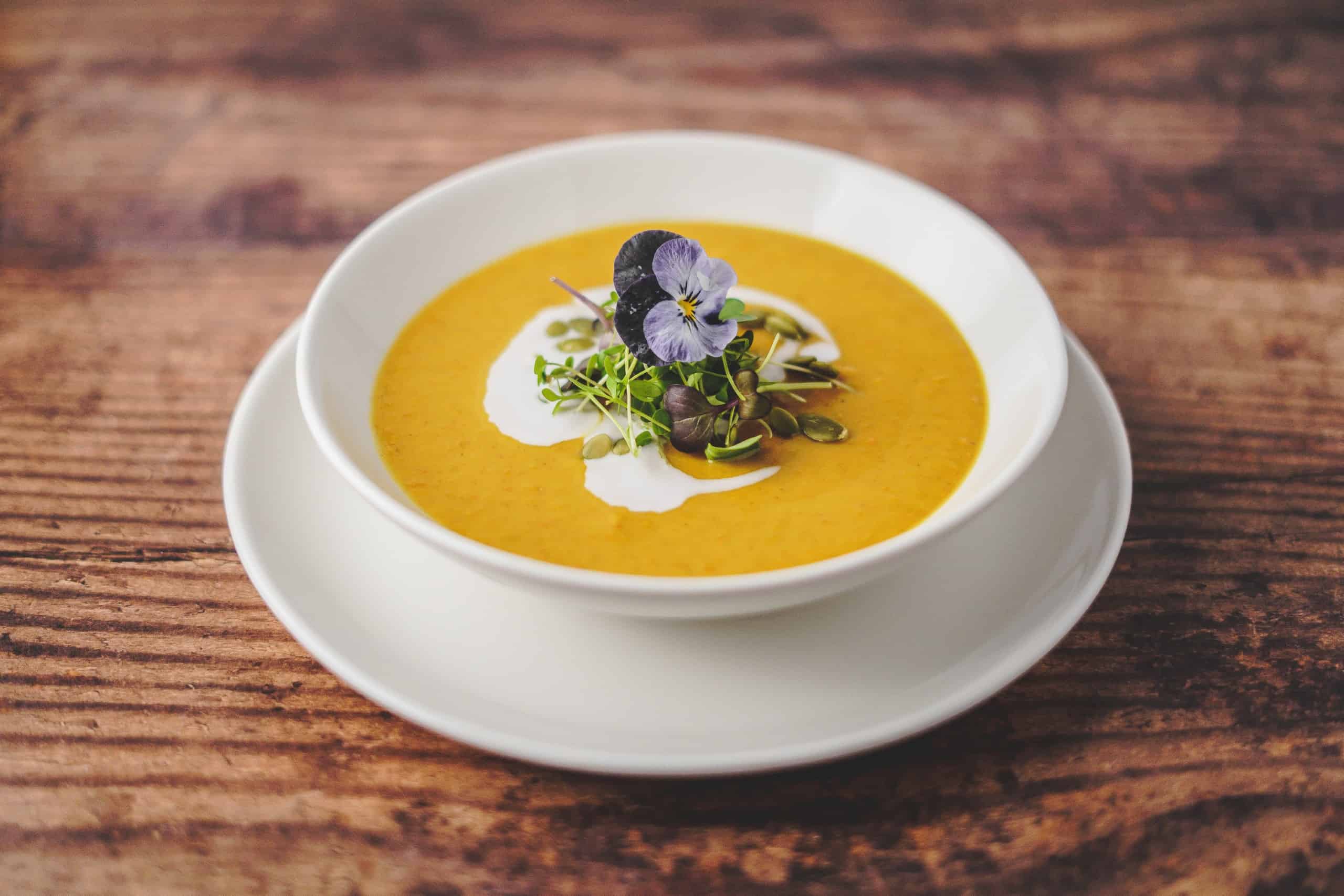 Spiced Squash Soup - beautiful yellow colour soup with cream swirl and topped with edible flowers