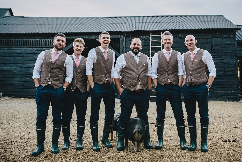 Groom and Grooms Men in Waistcoats and Wellington Boots with Piglet at Farm Wedding