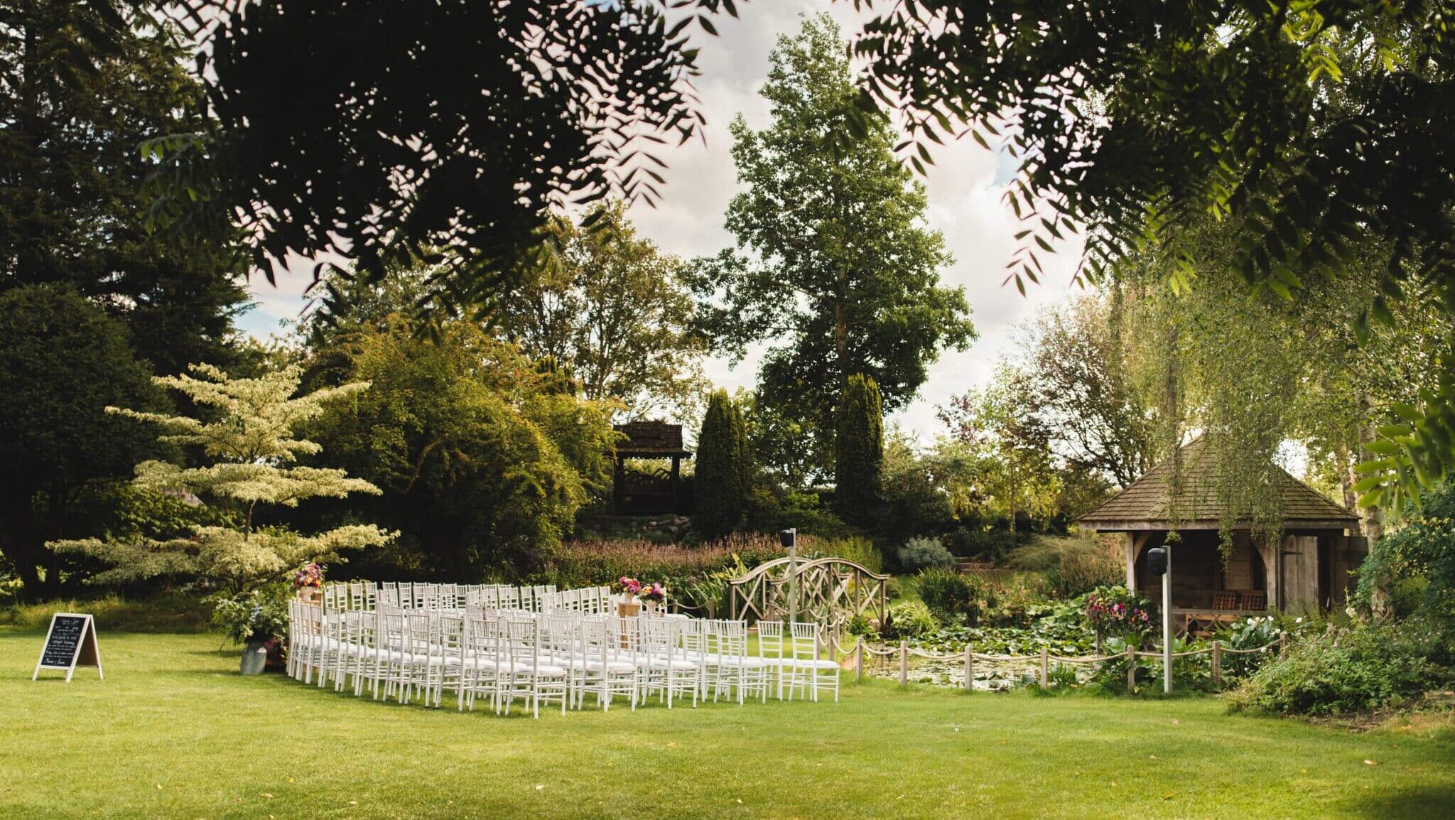 Beautiful secluded garden at countryside wedding venue set with white chairs on the lawns for a wedding ceremony on a sunny day