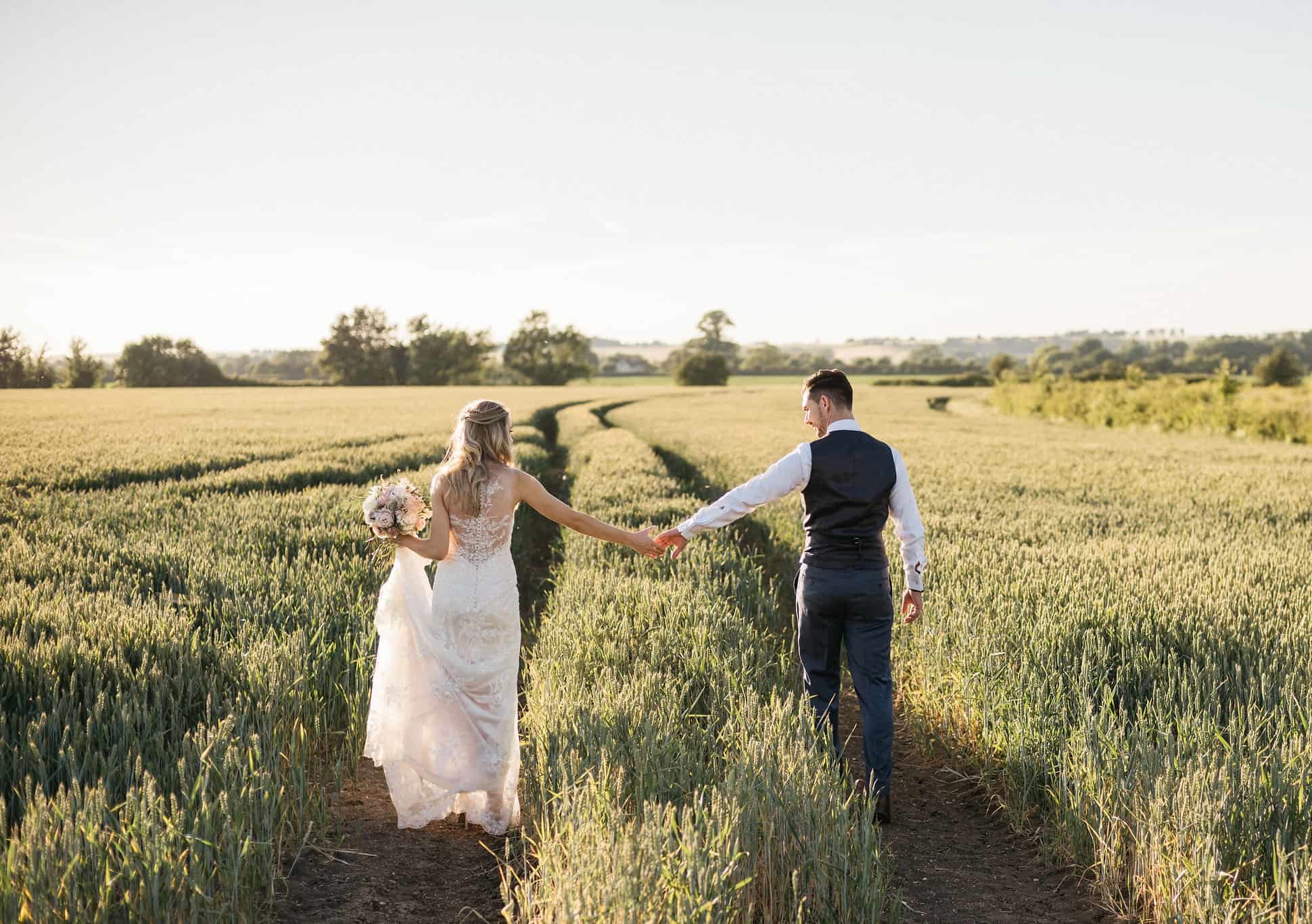 Bride and Groom on wedding day hold hands in field of corn