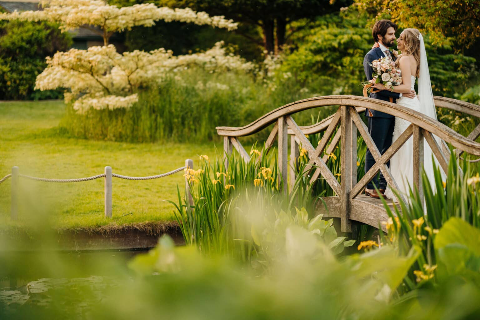 Bride and groom on bridge over pond at beautiful garden wedding venue