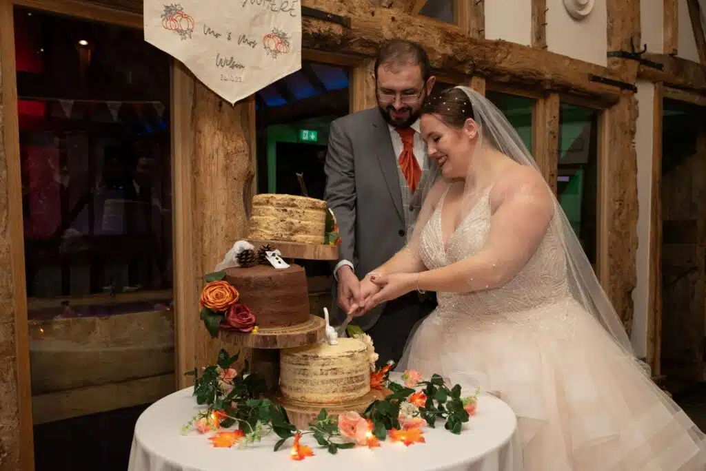 Bride and Groom cutting the cake in rustic Tudor Barn 