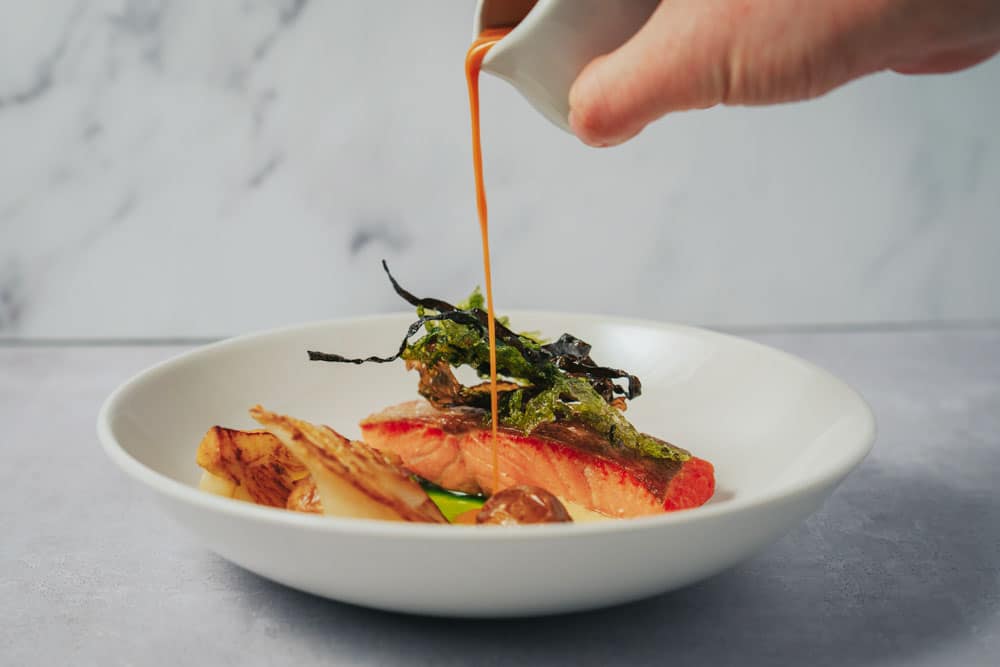 Roast Sea Trout fine dining wedding food with sauce being poured over dish