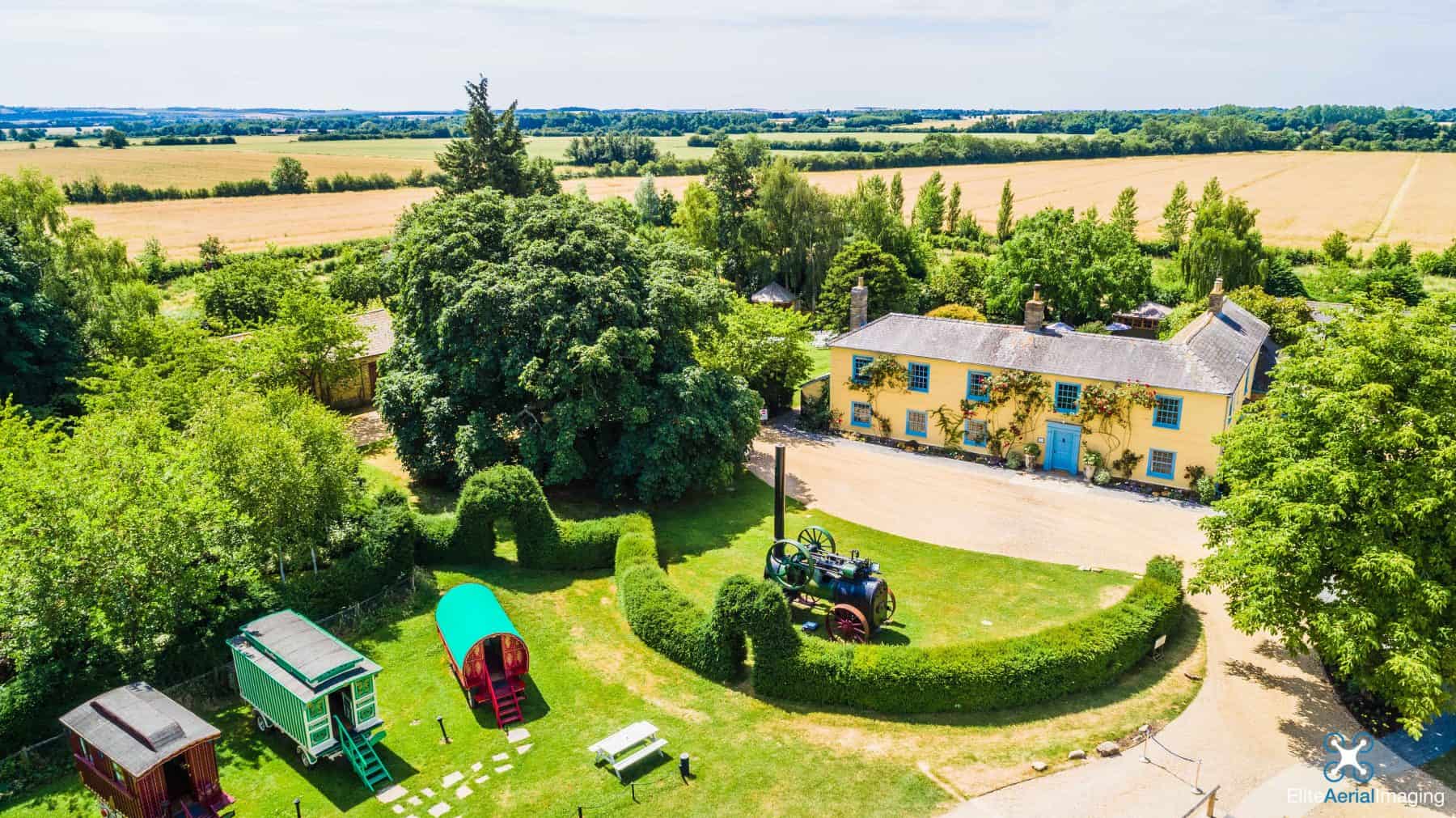 South Farm aerial view from above with pretty romany wagons and cream farmhouse with blue windows
