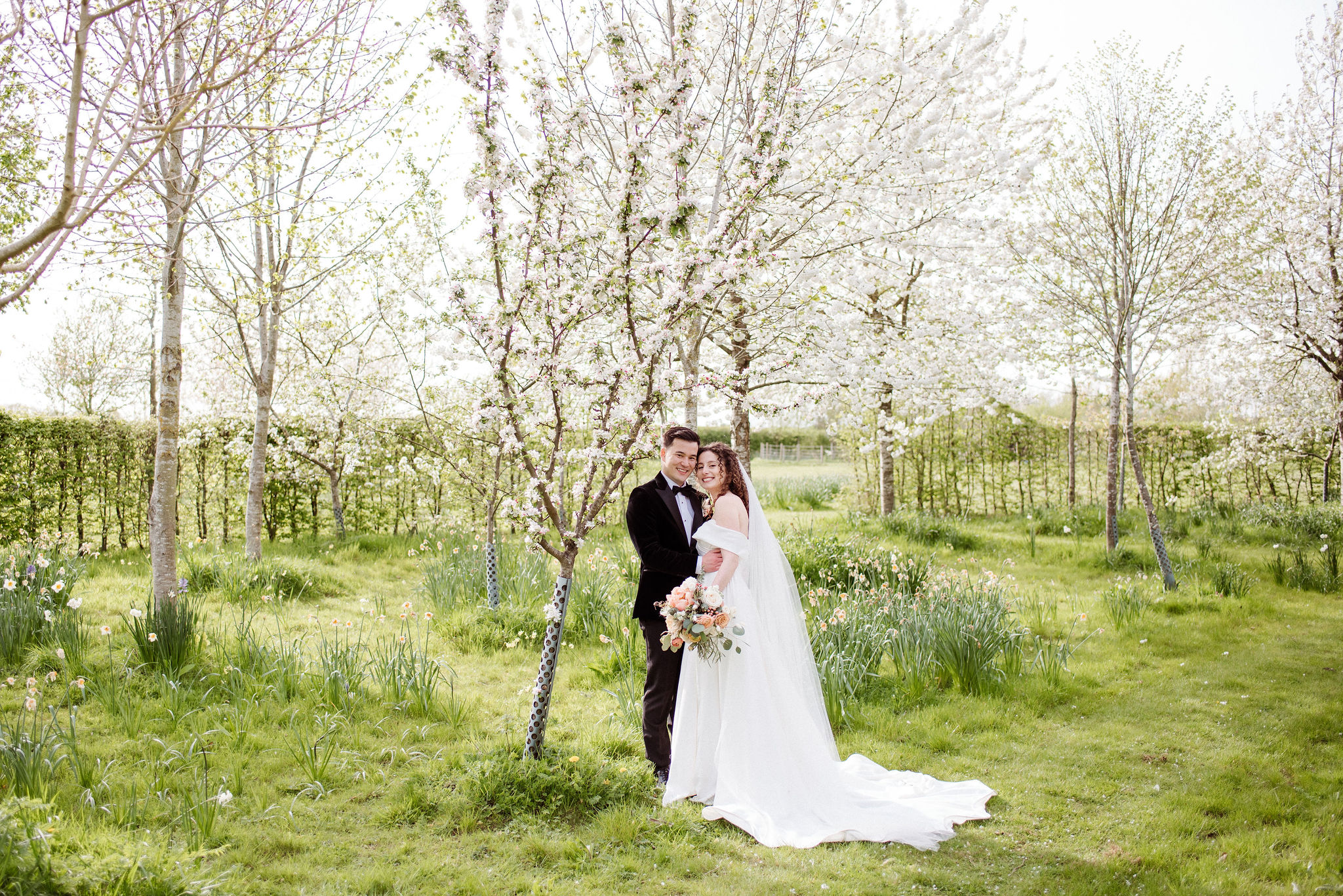 Bride and Groom on wedding day in green fields at farm wedding venue surrounded by trees with Spring Blossom